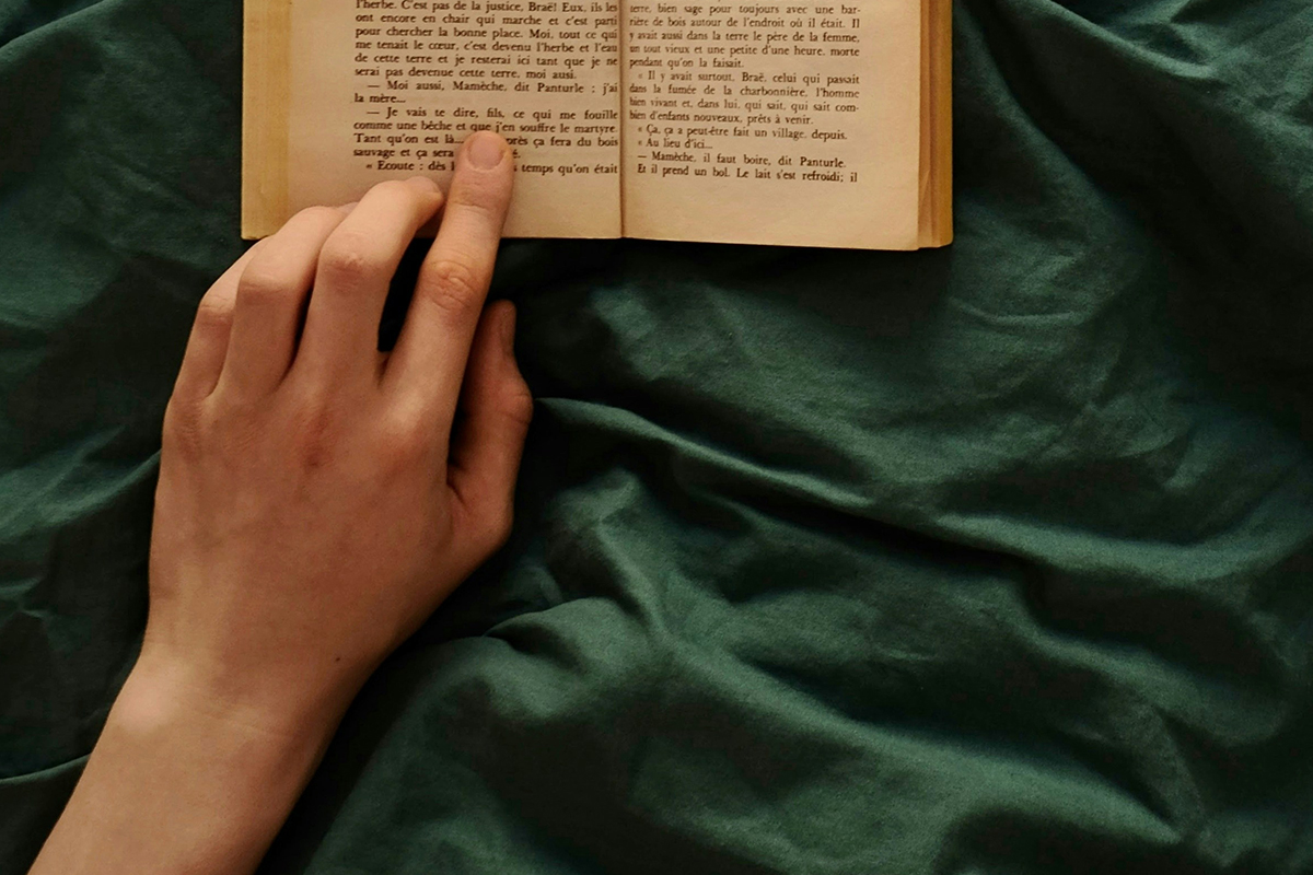 Sleep Tourism- Person reading in bed an old book wrapped in green bedhseets- Photo by Alexis Fauvet- Kai interio